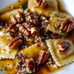 Butternut-Kürbis-Ravioli mit brauner Butter-Sauce und Pekannüssen auf einem Teller