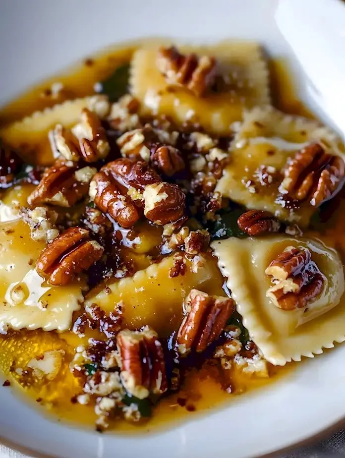 Butternut-Kürbis-Ravioli mit brauner Butter-Sauce und Pekannüssen auf einem Teller