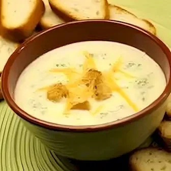 Schüssel mit Käse-Hasselback-Kartoffelsuppe, garniert mit frischen Kräutern