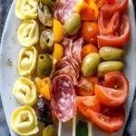 Italienische Antipasto-Spieße mit Tortellini und Oliven auf einem Teller.