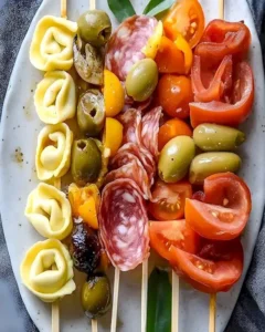 Italienische Antipasto-Spieße mit Tortellini und Oliven auf einem Teller.