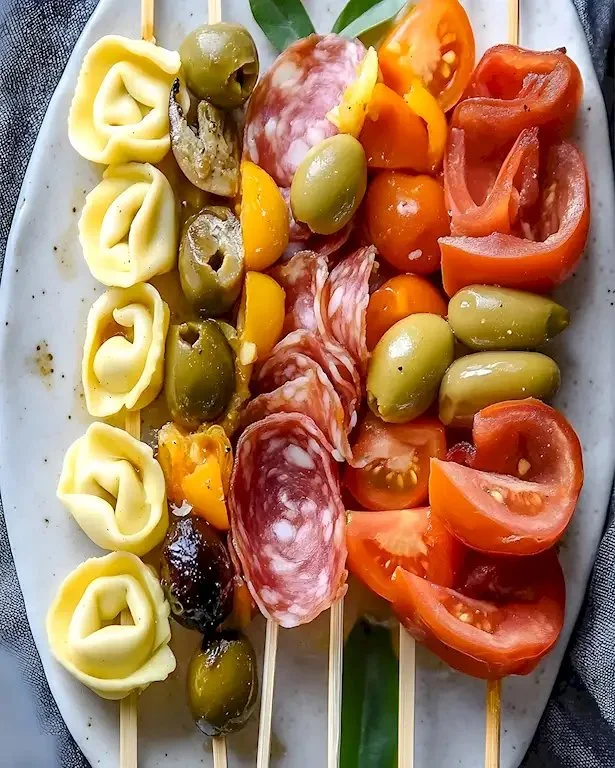 Italienische Antipasto-Spieße mit Tortellini und Oliven auf einem Teller.